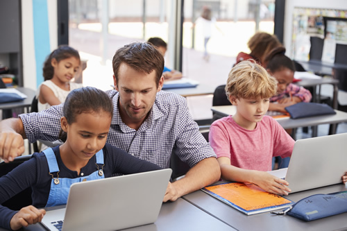 Digital learning has limitless possibilities--get some inspiration from how these educators are using edtech tools in their classrooms, like this male teacher helping students on laptops in the classroom.