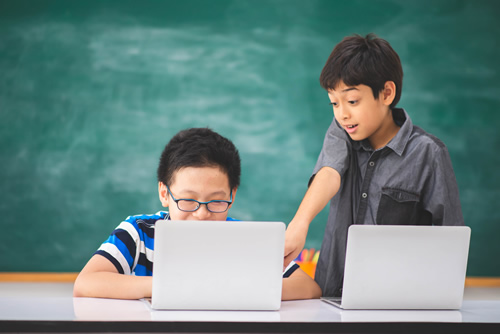 These two boys on laptops in a classroom demonstrate how 1:1 initiatives can be successful.